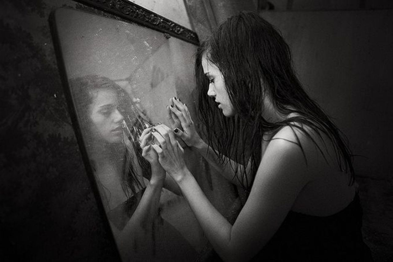 Giovane donna livisa vicino a specchio su sfondo scuro, primo